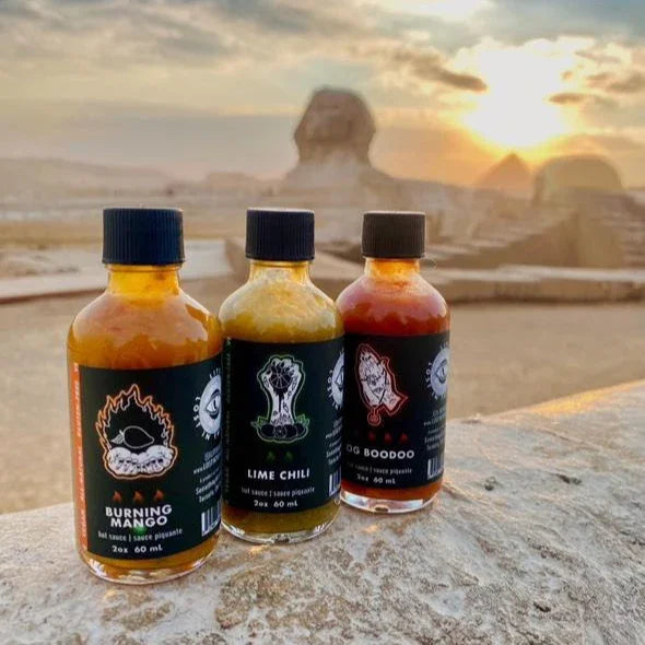 Three LITS hot sauces in front of the Sphinx and pyramids in Egypt at sunset.