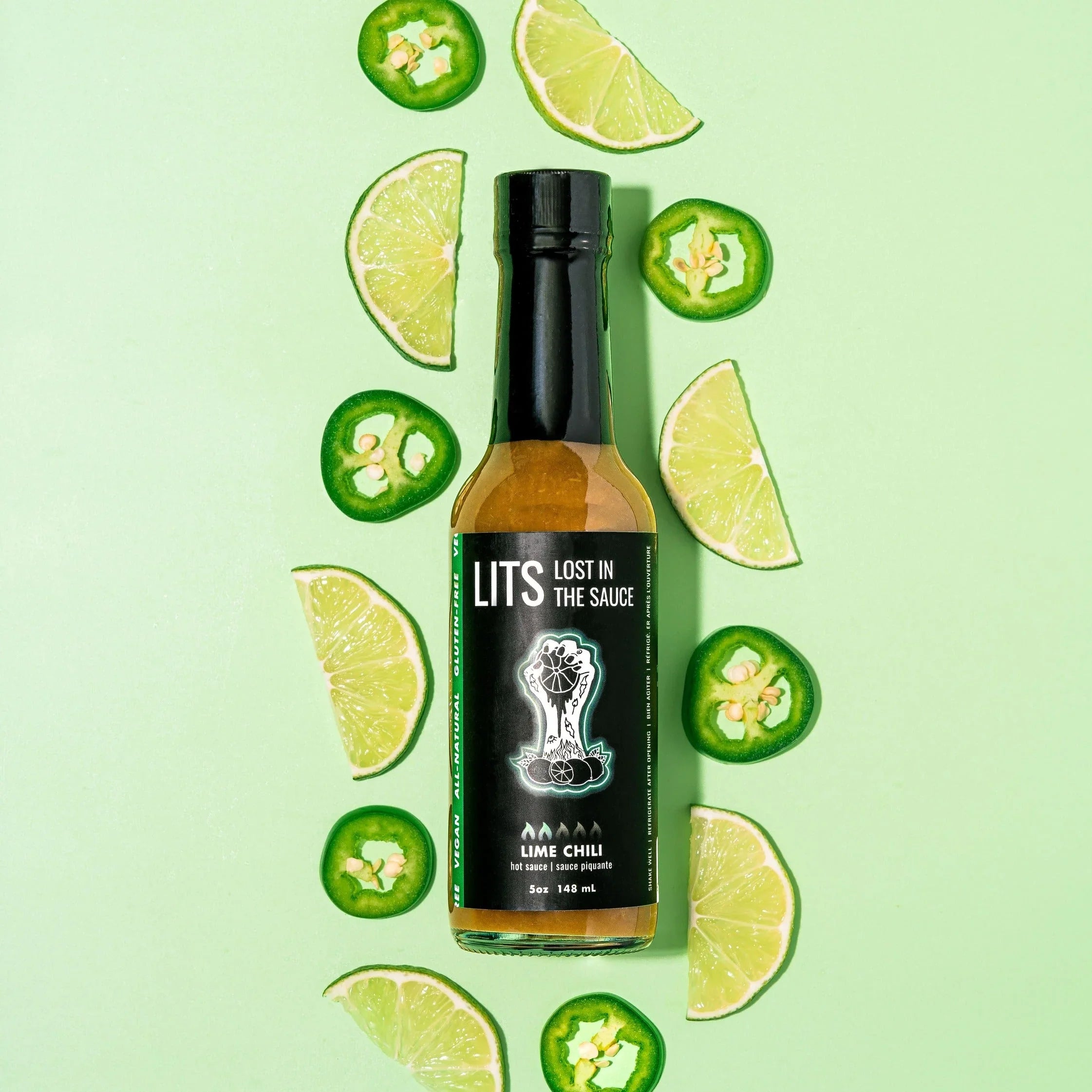 LITS Lime Chili hot sauce bottle on green background with lime wedges and chili slices