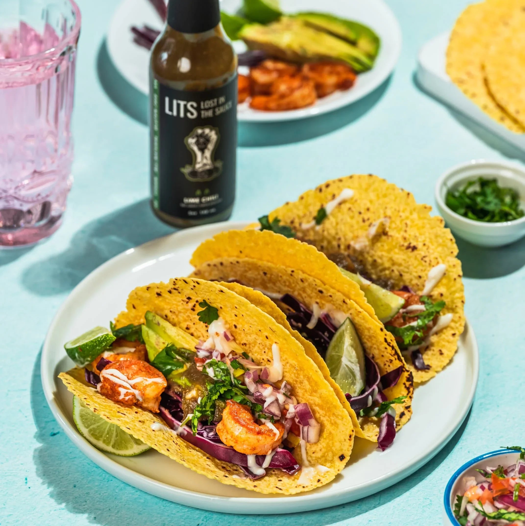 Shrimp tacos with lime, cabbage, and sauce on corn tortillas, LITS Lime Chili hot sauce nearby