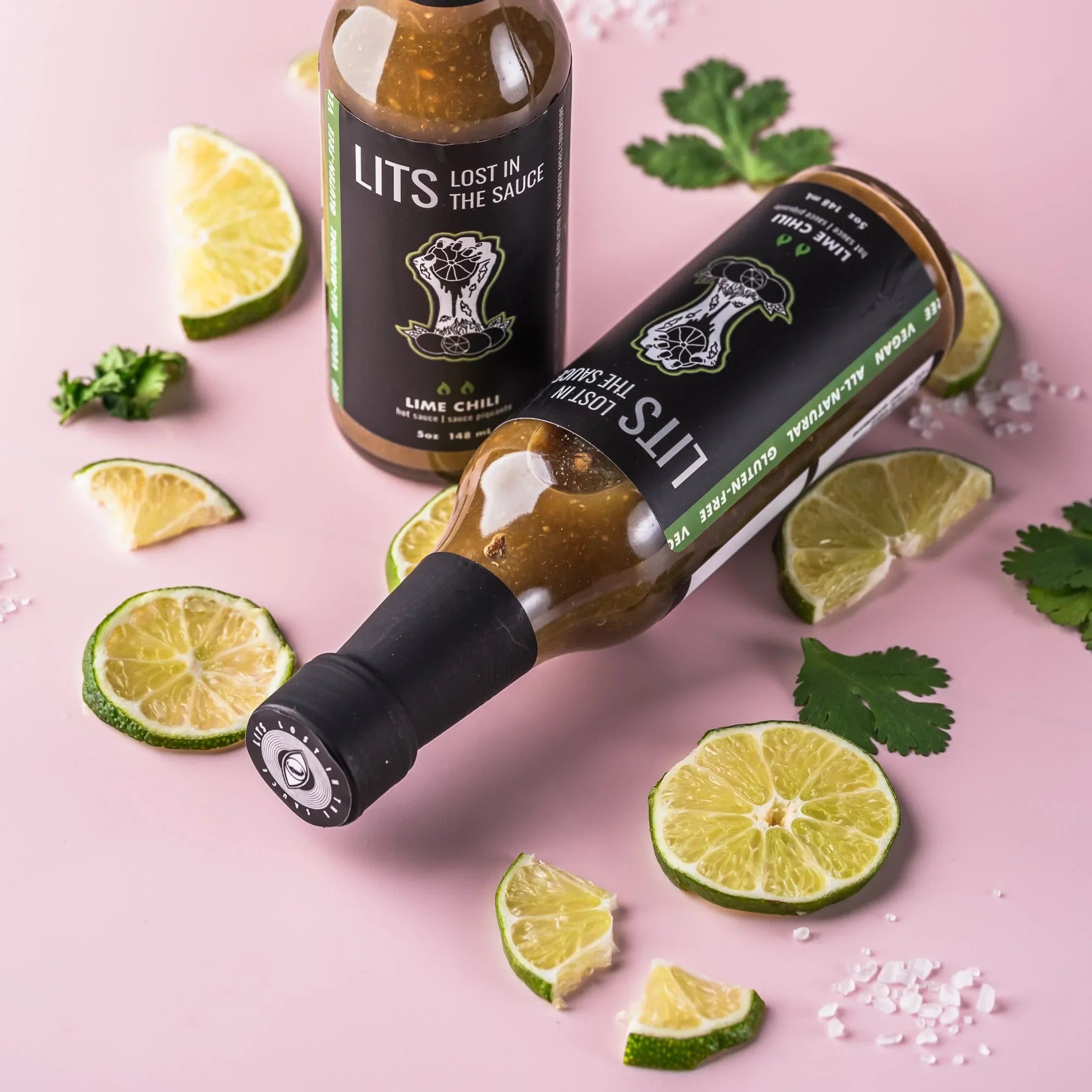 LITS Lime Chili hot sauce bottles with lime slices and cilantro on a pink background