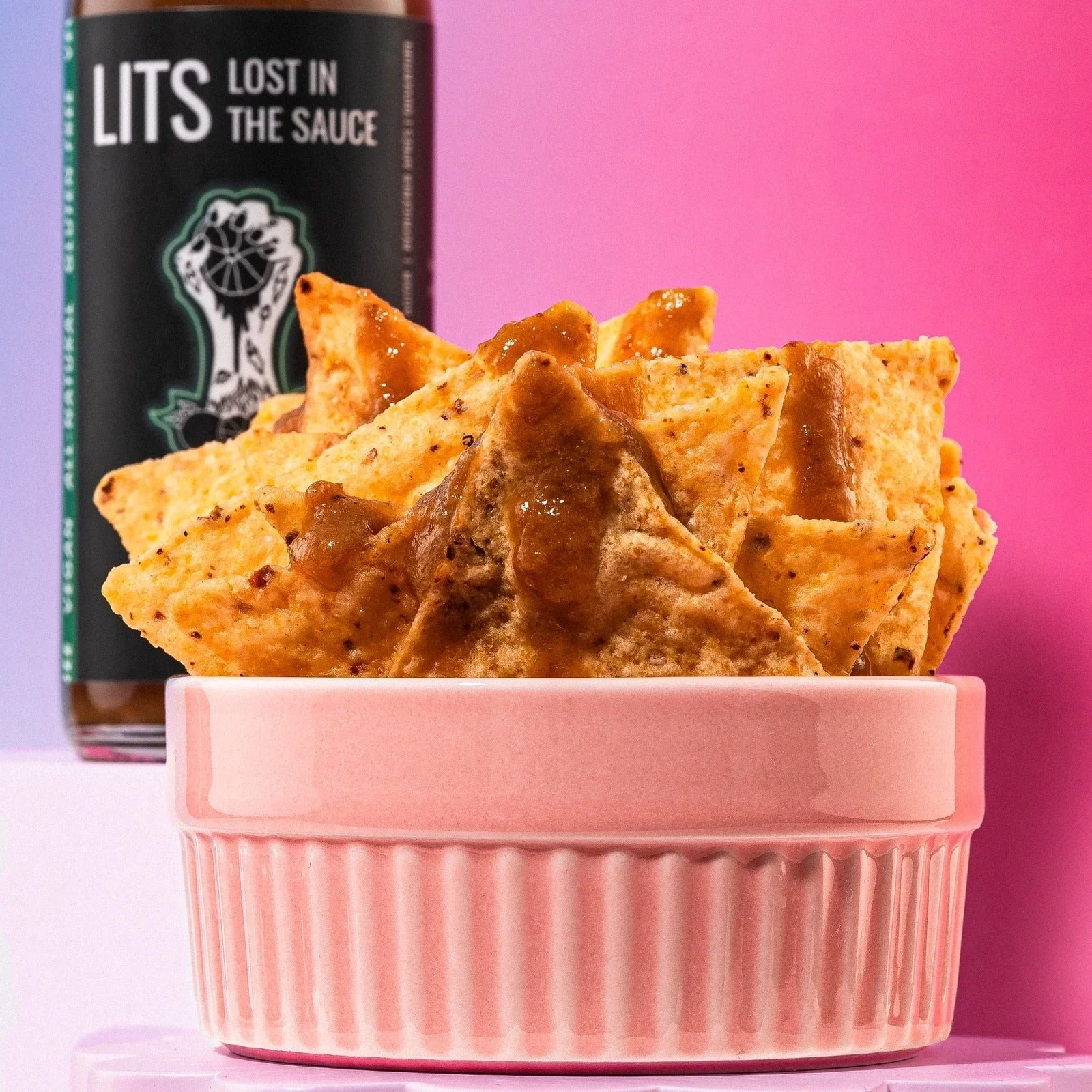 Nachos with chili lime sauce in a pink bowl, LITS Lost in the Sauce bottle in background