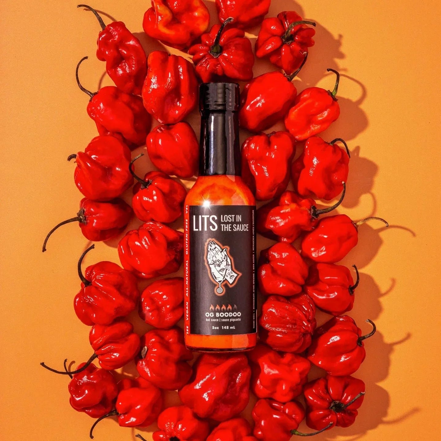 LITS OG Boodoo hot sauce bottle surrounded by red peppers on orange background