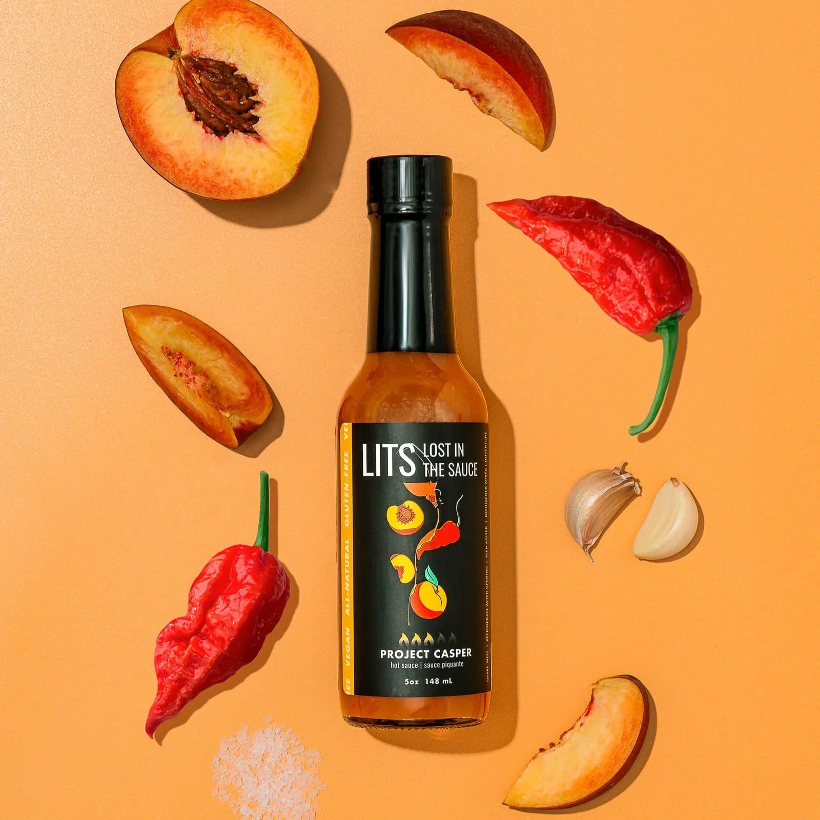 LITS Project Casper hot sauce bottle with peach slices, garlic cloves, red peppers, and salt on orange background