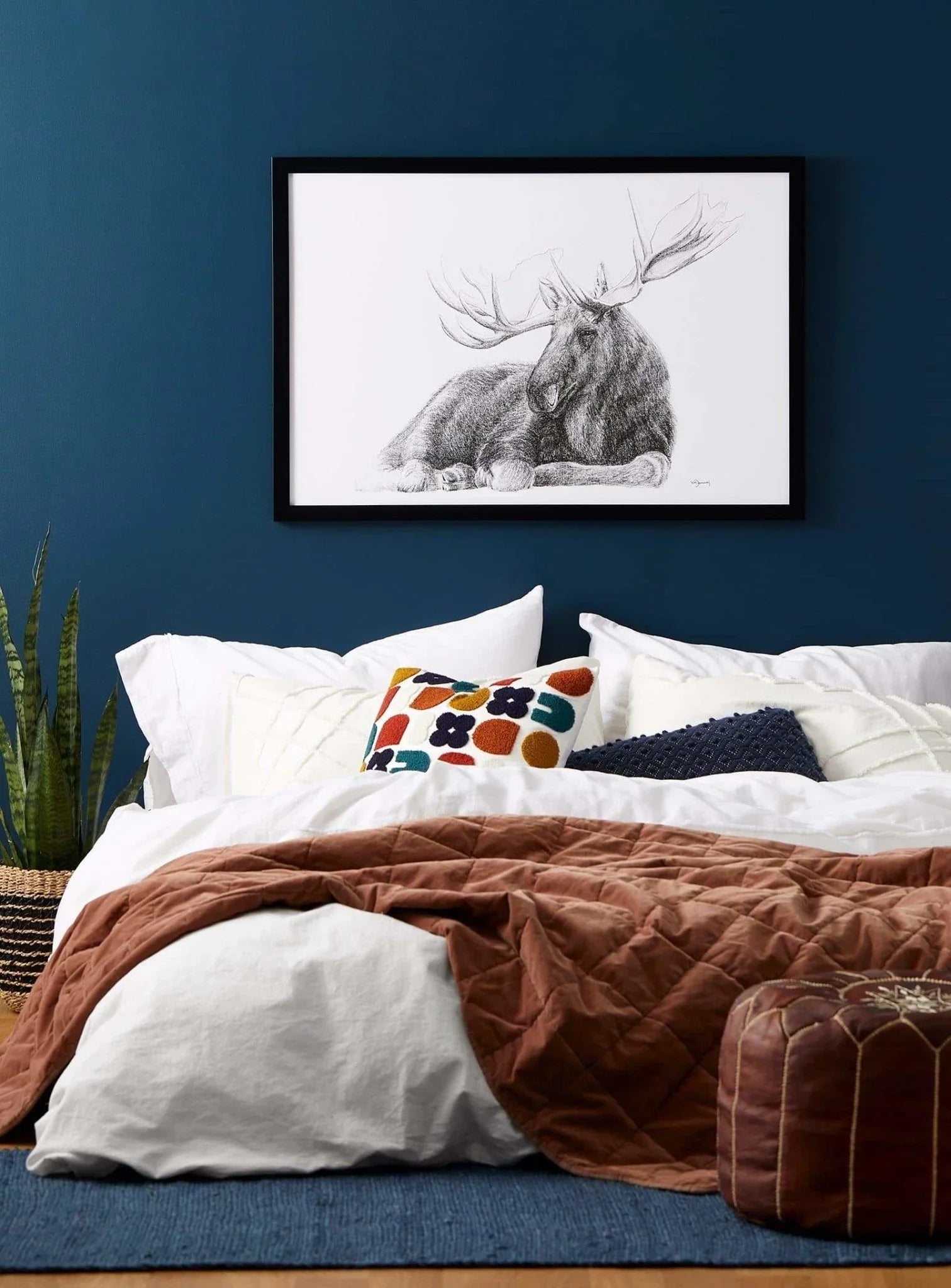Cozy bedroom with white bedding, patterned pillows, and moose wall art on a navy wall