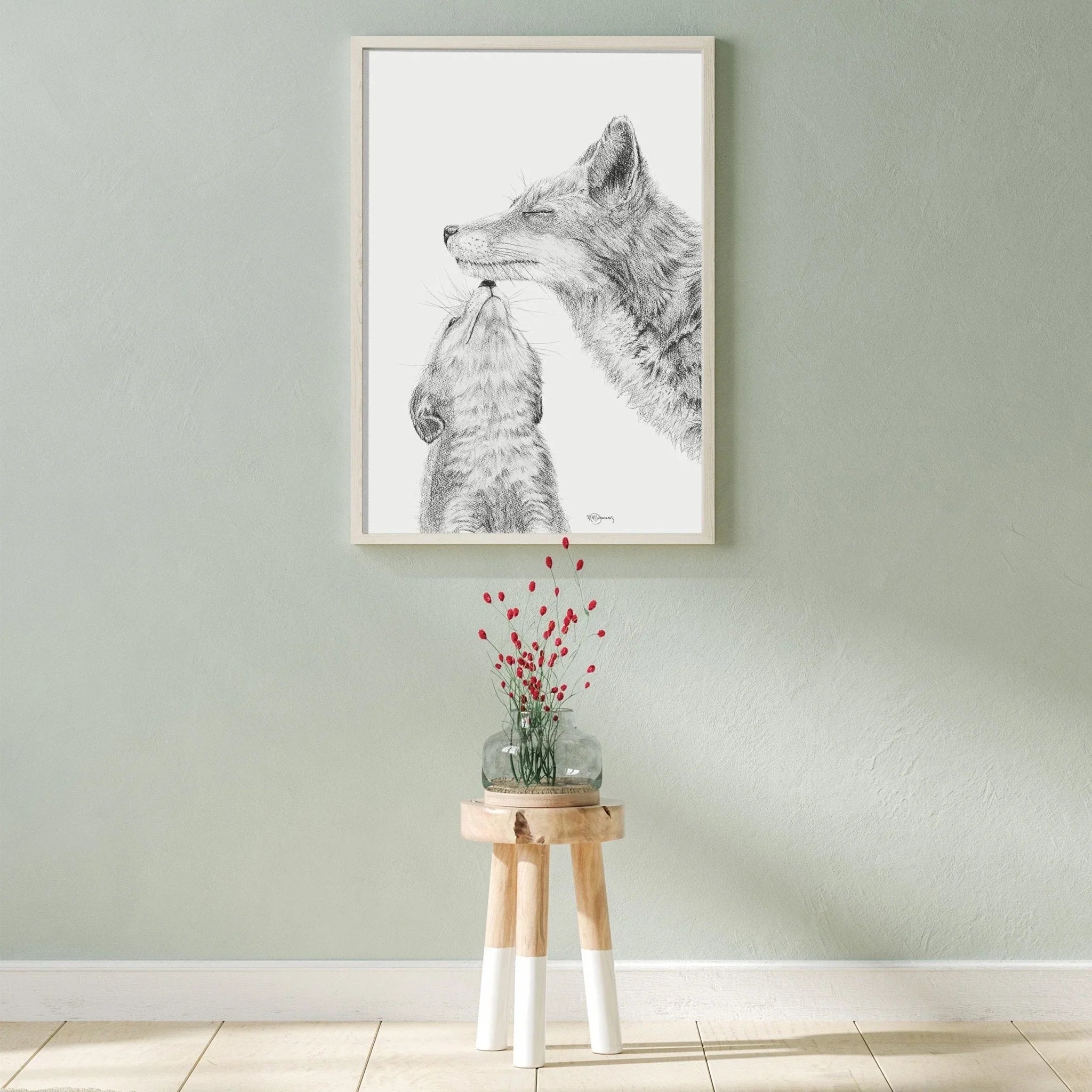Framed black and white fox and baby fox drawing on wall above wooden stool with vase