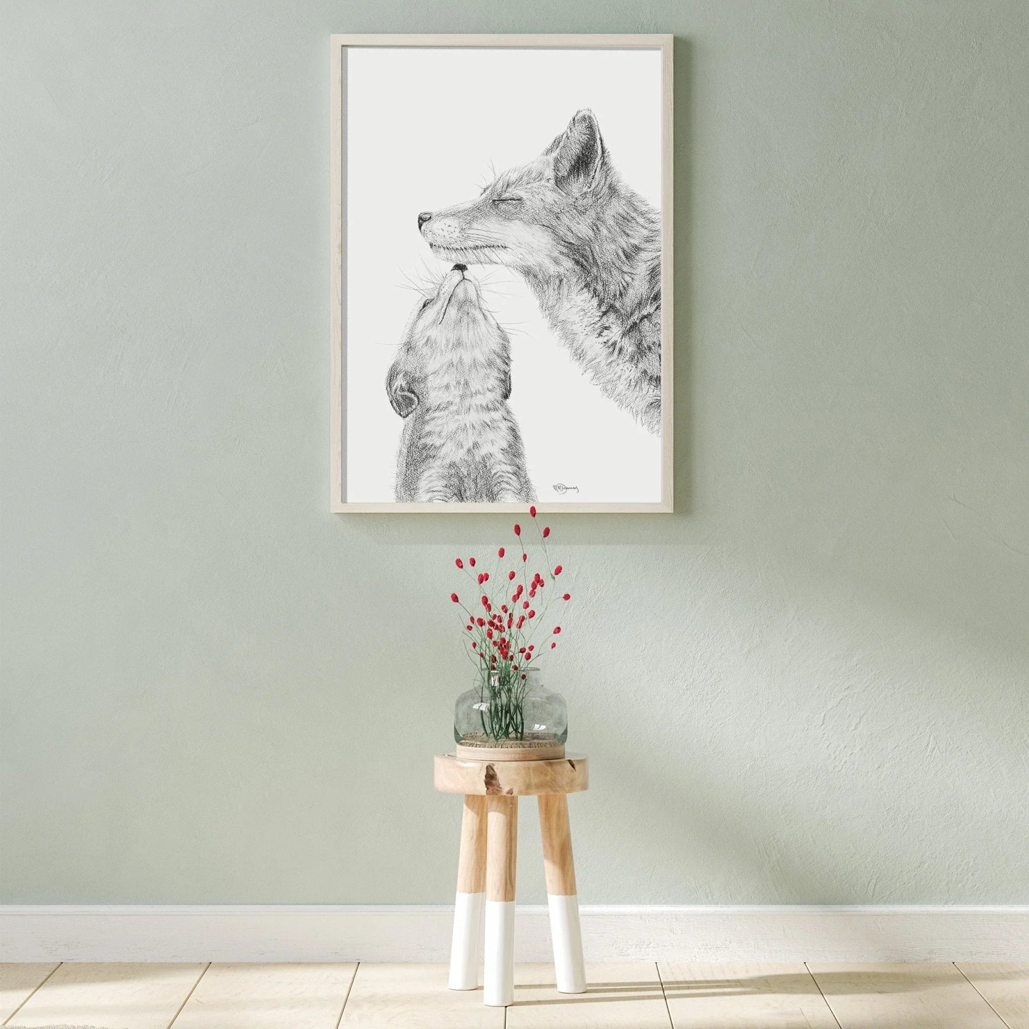Framed black and white fox and baby fox drawing on wall above wooden stool with vase