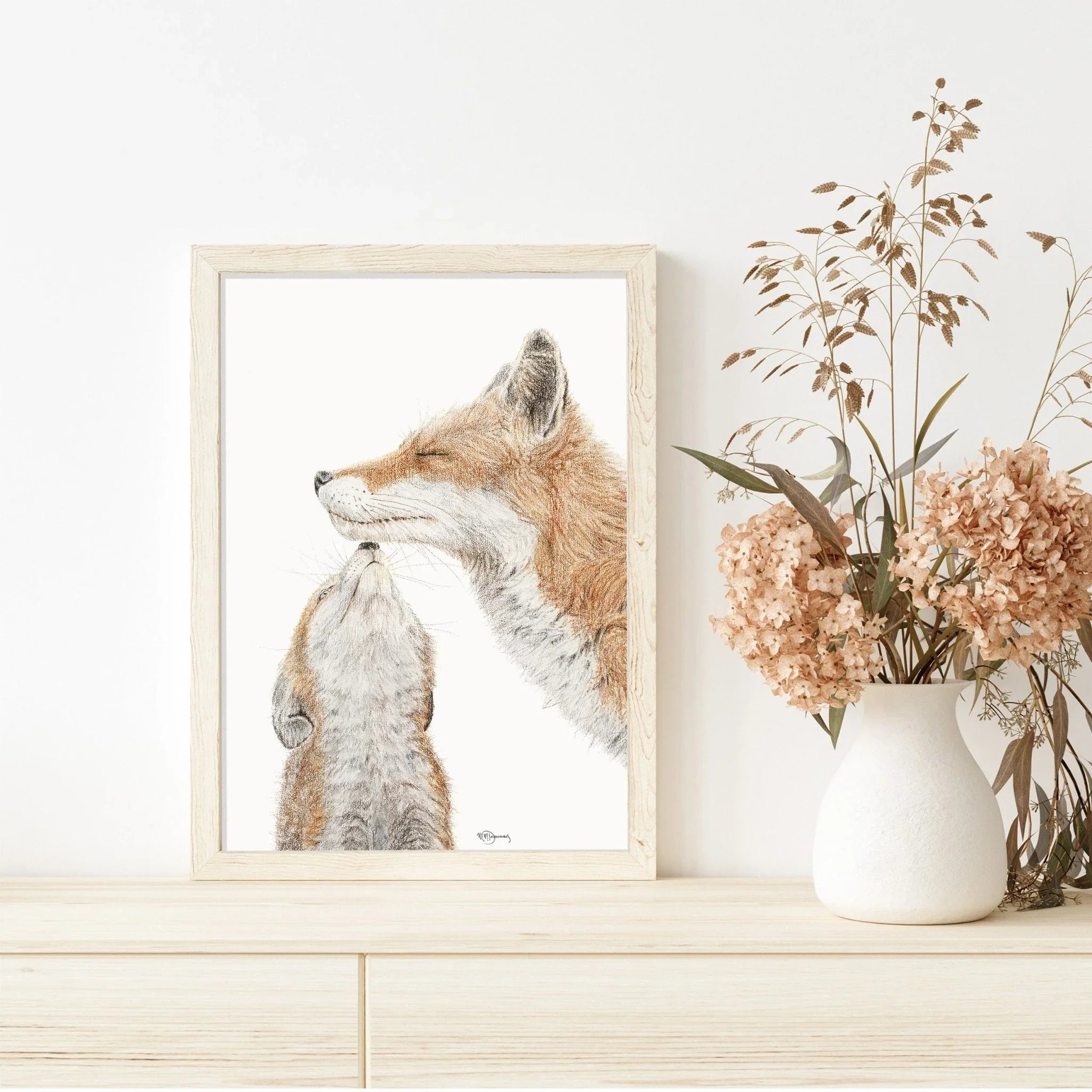 Framed watercolor art of mama fox and baby fox on wood dresser beside dried flowers in vase