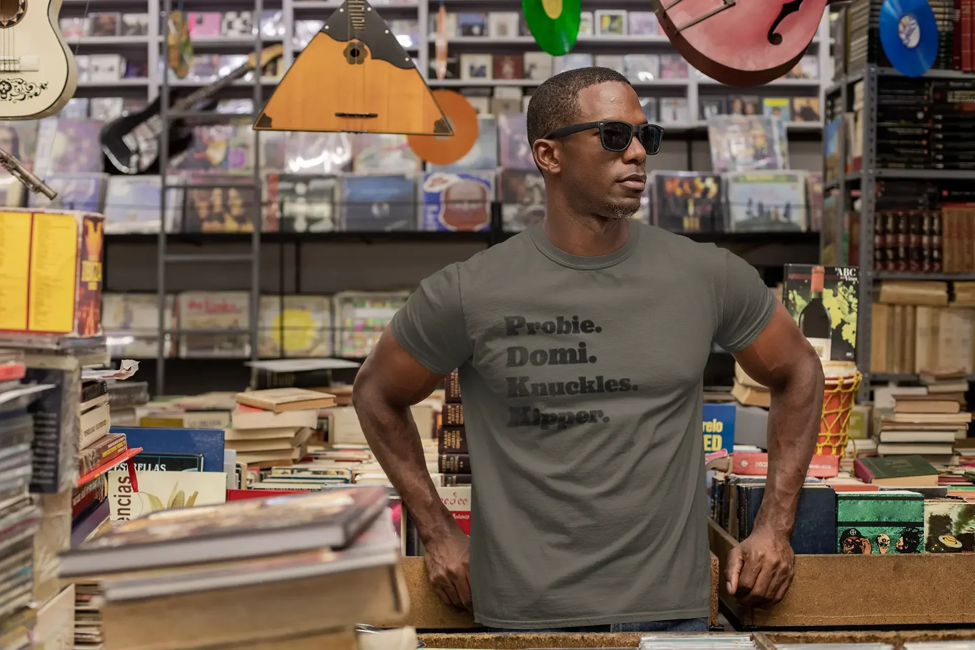 Man in sunglasses and printed t-shirt standing in a vintage bookstore with records and guitars