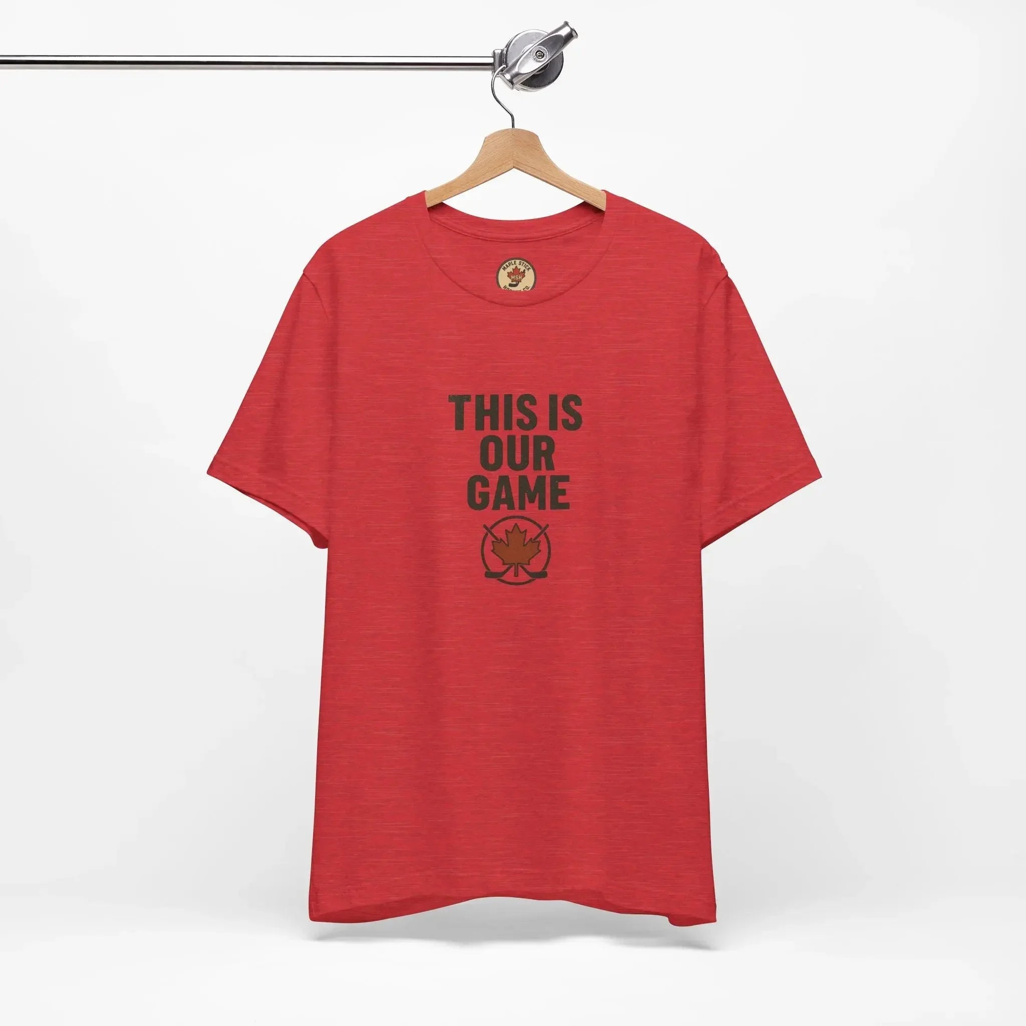 Red t-shirt with 'This Is Our Game' and maple leaf graphic hanging on wooden hanger