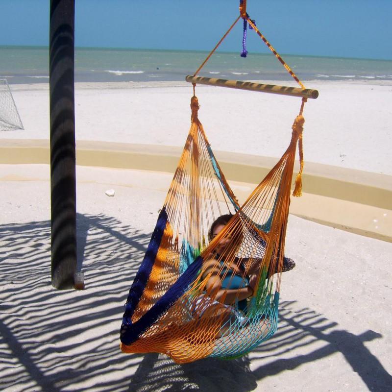 Person relaxing in a colorful hammock chair on a sandy beach with ocean view