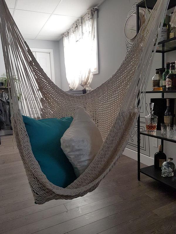 Mayan hanging chair indoors with blue and white pillows, near bar cart and window