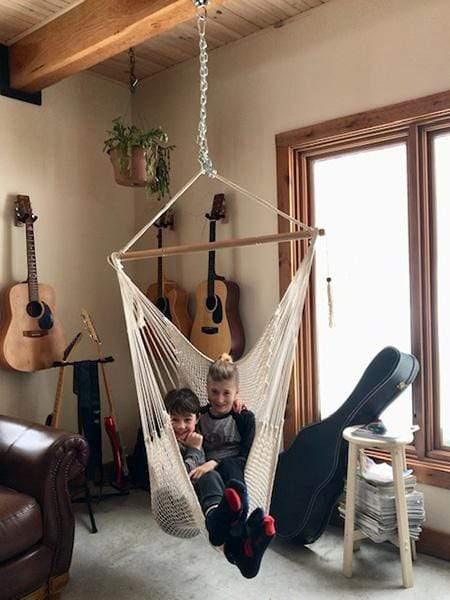 Two children sitting in a white Mayan hammock chair in a cozy music room with guitars.