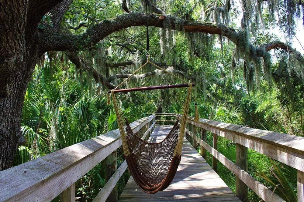 Mayan hammock chair in chocolate color hanging on a wooden deck in a lush, green forest
