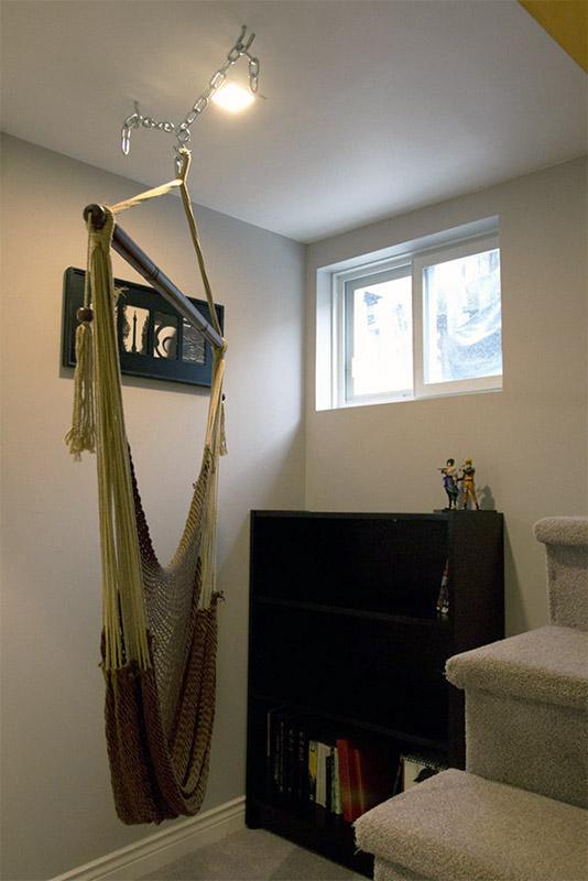 Mayan hanging chair suspended from ceiling in a cozy indoor reading nook by a window and bookshelf.