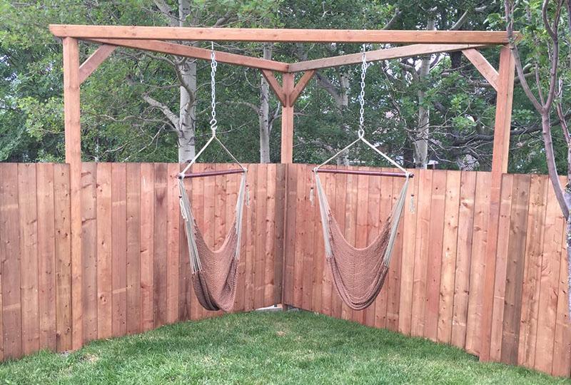 Two Mayan hanging chairs suspended from a wooden frame in a fenced backyard