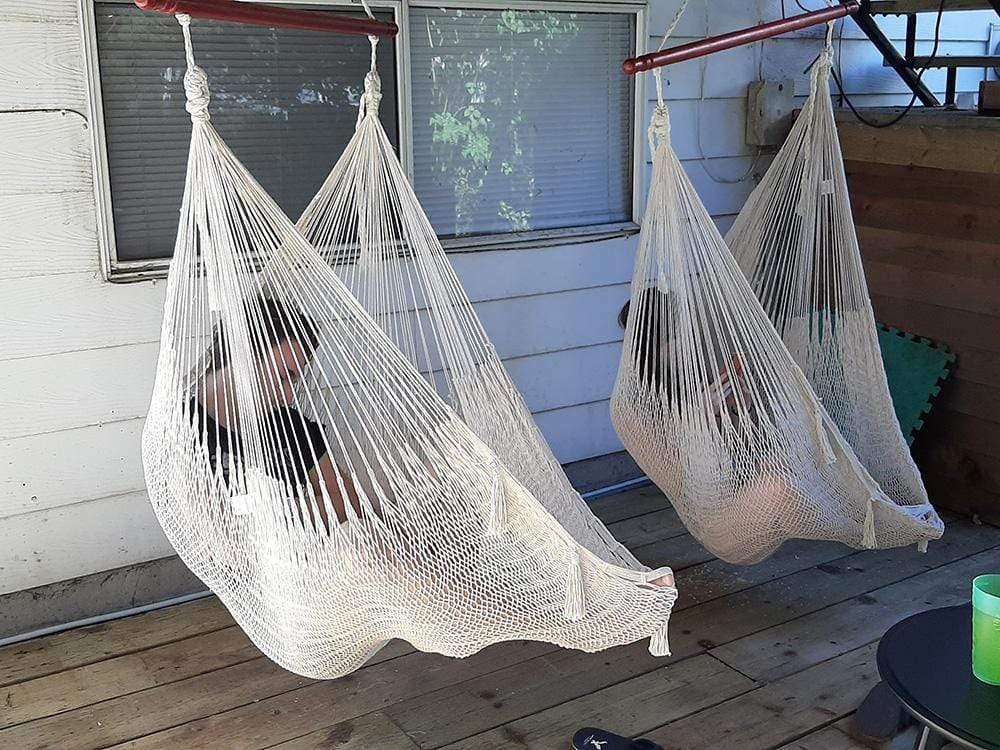 Two white Mayan hammock chairs with people sitting on a wooden porch, outdoor seating