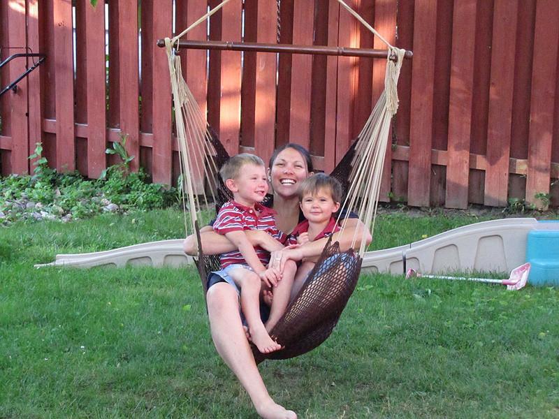 Woman and two kids sitting in a Mayan hammock chair in a backyard with wooden fence