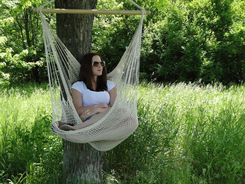 Woman relaxing in a hanging hammock chair outdoors, surrounded by green trees and grass