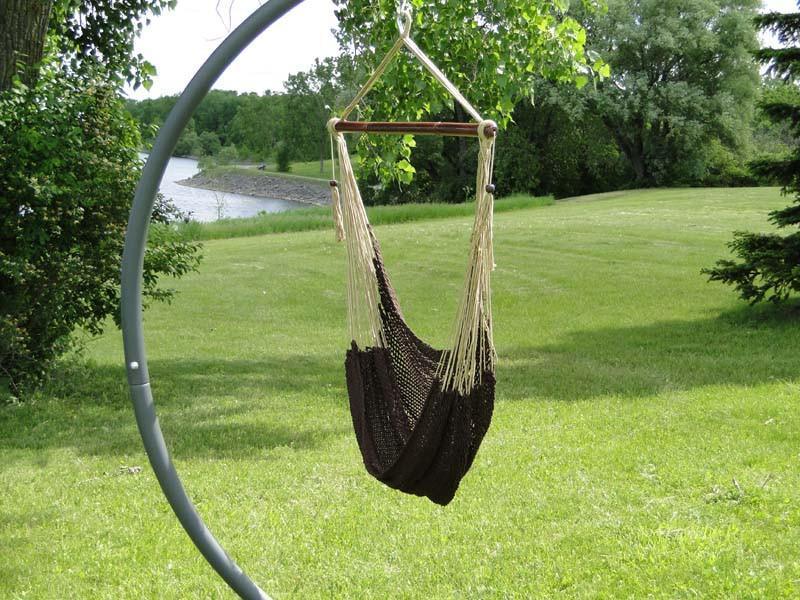 Brown hanging hammock chair on metal stand in a green backyard near a river