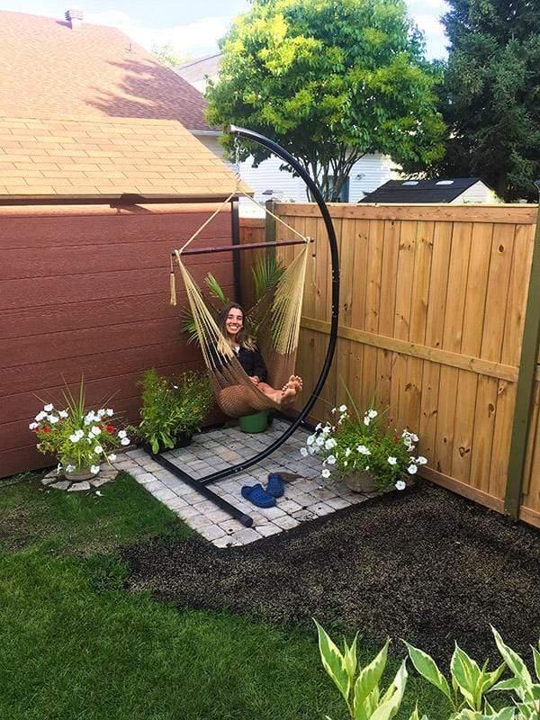 Mayan hammock chair on black metal stand in garden corner with flowers and a wooden fence