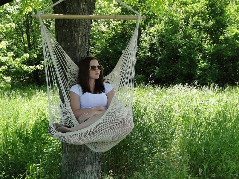 Woman relaxing in a hammock chair hung from a tree in a green outdoor setting