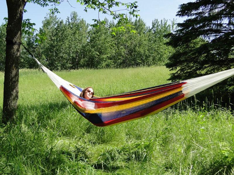Woman relaxing in a colorful Mayan hammock tied between trees in a grassy meadow
