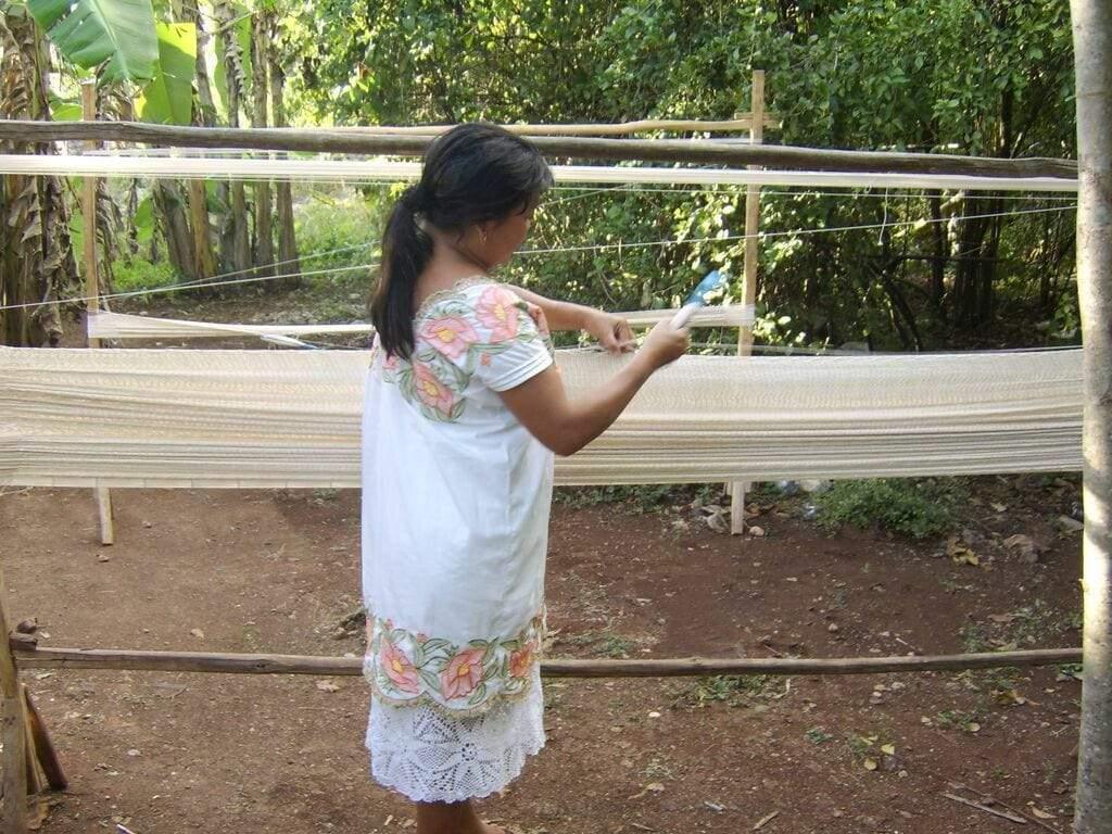 Mayan woman weaving traditional textile outdoors using backstrap loom in rural setting