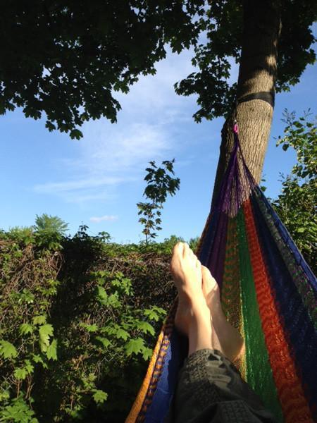 Person relaxing in a colorful Mayan hammock tied to a tree outdoors on a sunny day