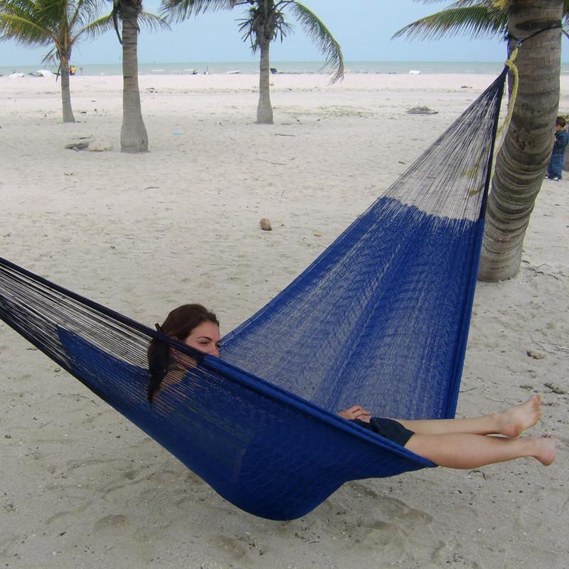 Woman relaxing in a blue Mayan hammock tied between palm trees on a sandy beach