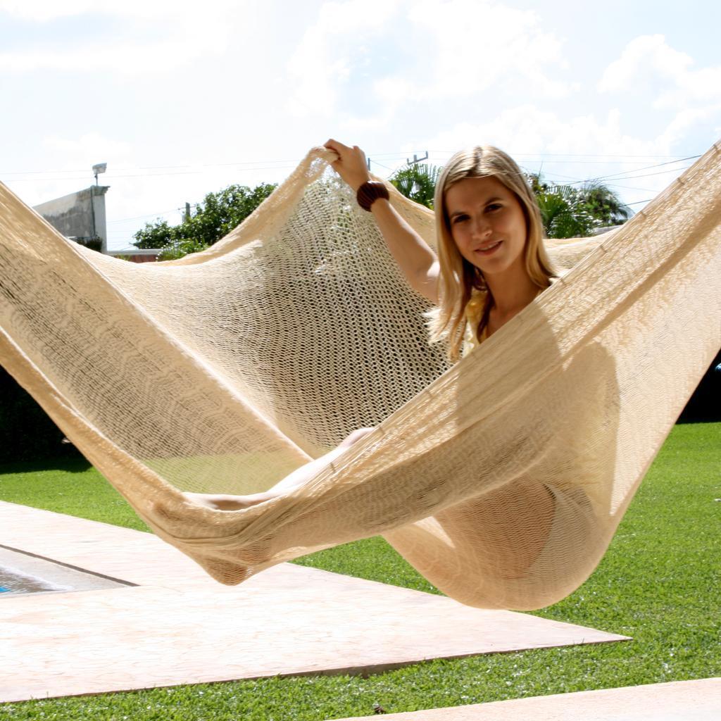 Woman relaxing in a natural cotton Mayan hammock outdoors on green lawn under sunny sky