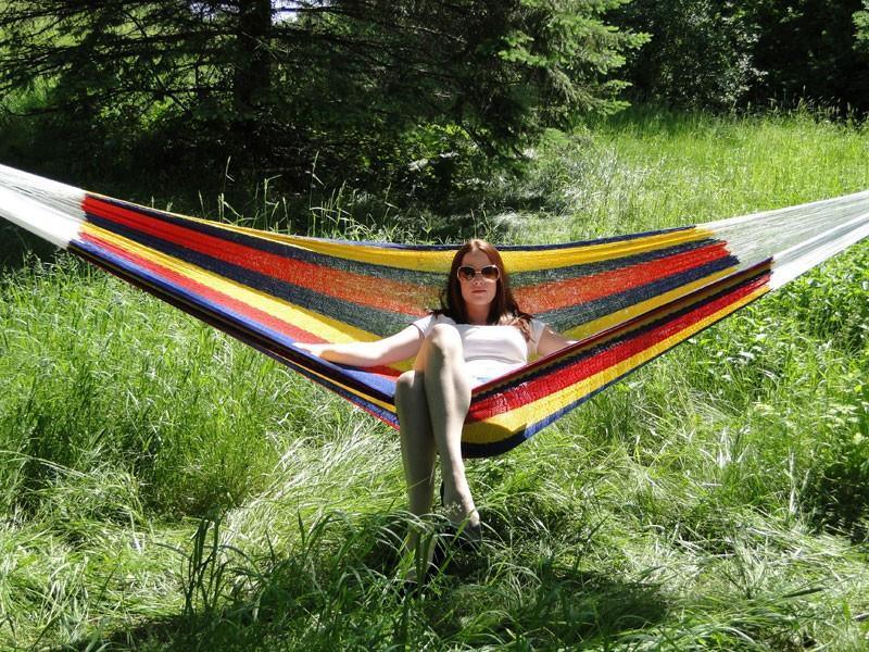 Woman relaxing in a large colorful Mayan double hammock outdoors on green grass