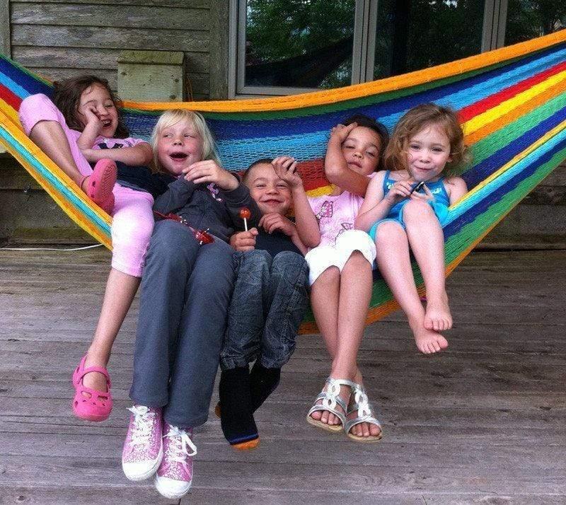 Five children relax in a colorful Mayan hammock on a wooden porch outdoors
