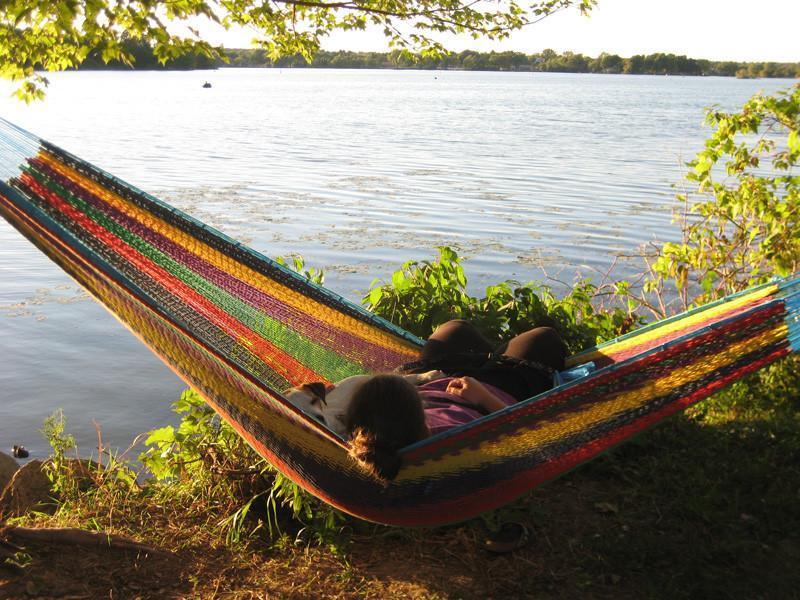Person relaxing in a colorful Mayan hammock beside a calm lakeside under tree shade