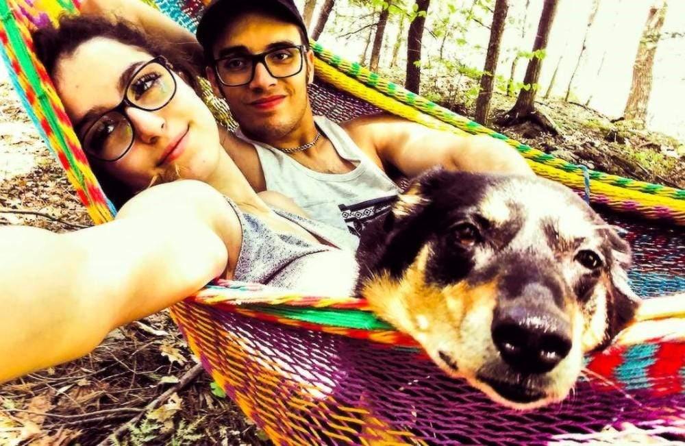 Two people and a dog relaxing in a colorful Mayan hammock in a forest setting