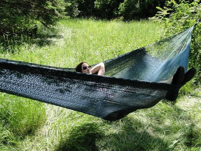 Woman relaxing in an XL thick cord Mayan hammock outdoors on green grass