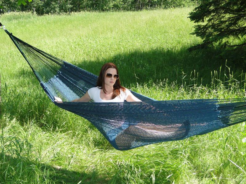Woman relaxing in an XL thick cord Mayan hammock outdoors on a sunny grassy field