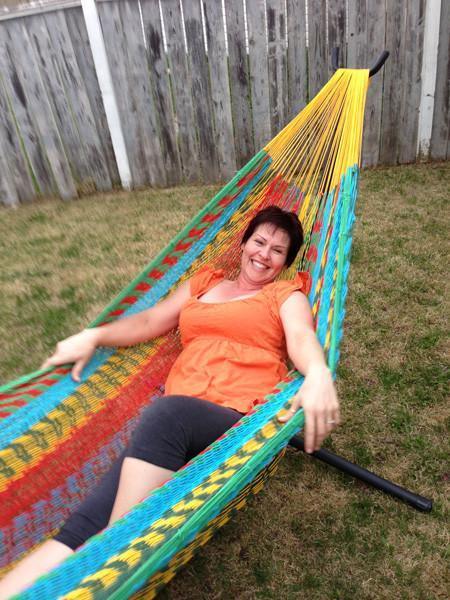 Woman relaxing in a colorful extra-large Mayan hammock on a metal stand in a backyard