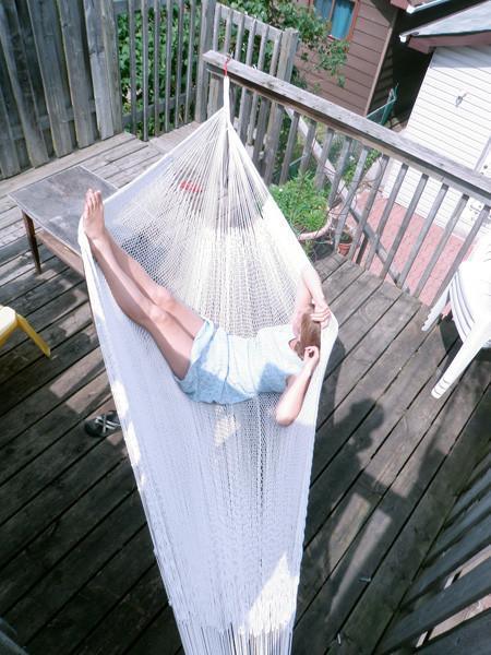 Person relaxing in a white Mayan hammock on a wooden deck outdoors