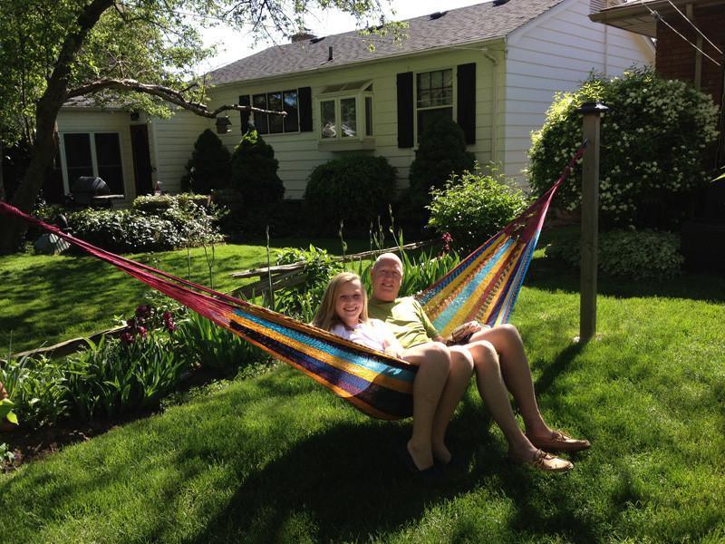 Two people relaxing in a colorful Mayan hammock in a sunny backyard garden