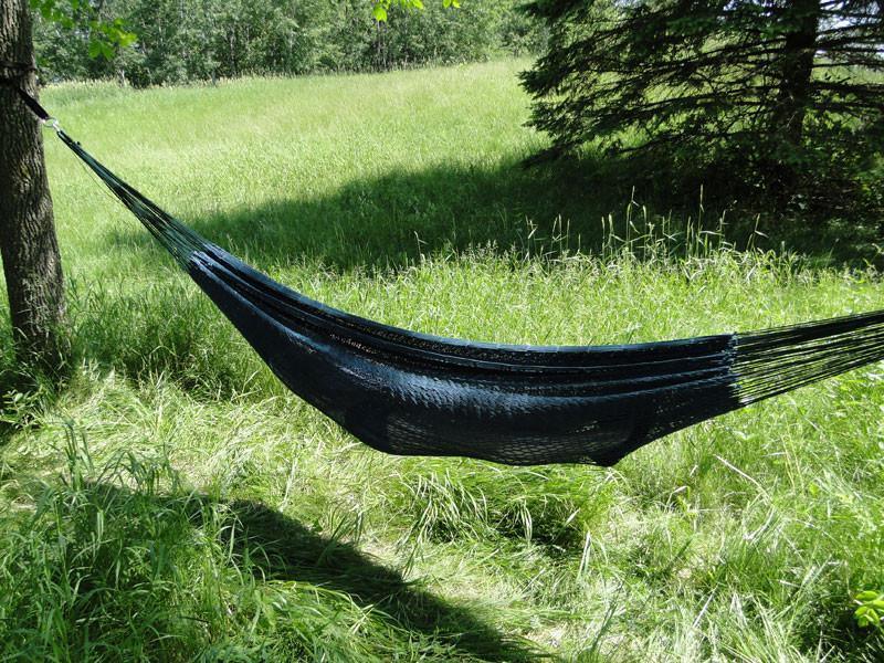 XL black Mayan hammock with thick cord hanging between trees in a grassy outdoor setting