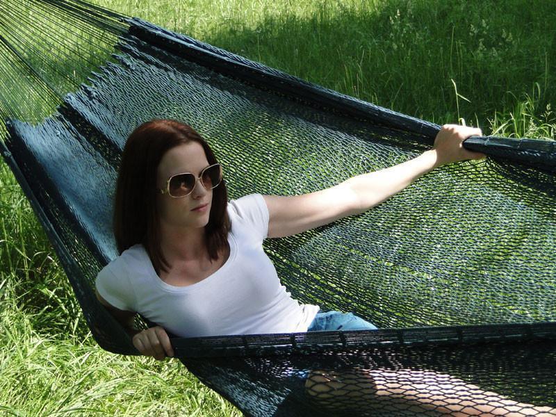 Woman relaxing in extra large Mayan hammock with thick cord outdoors on green grass