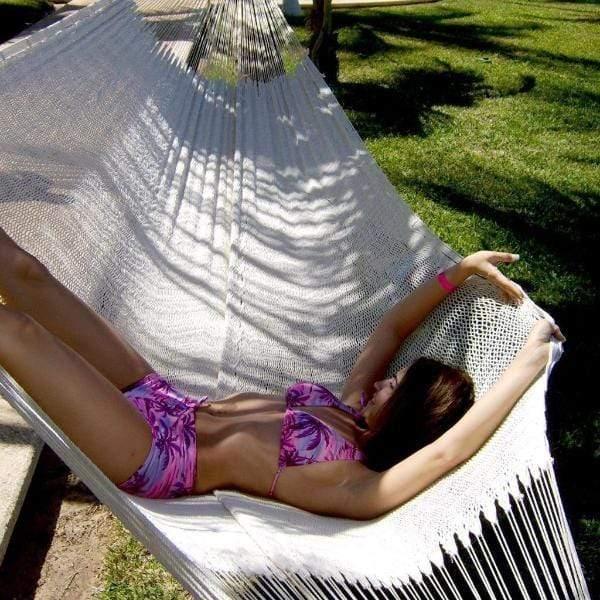 Woman relaxing on thick cotton XL natural hammock outdoors on green grass