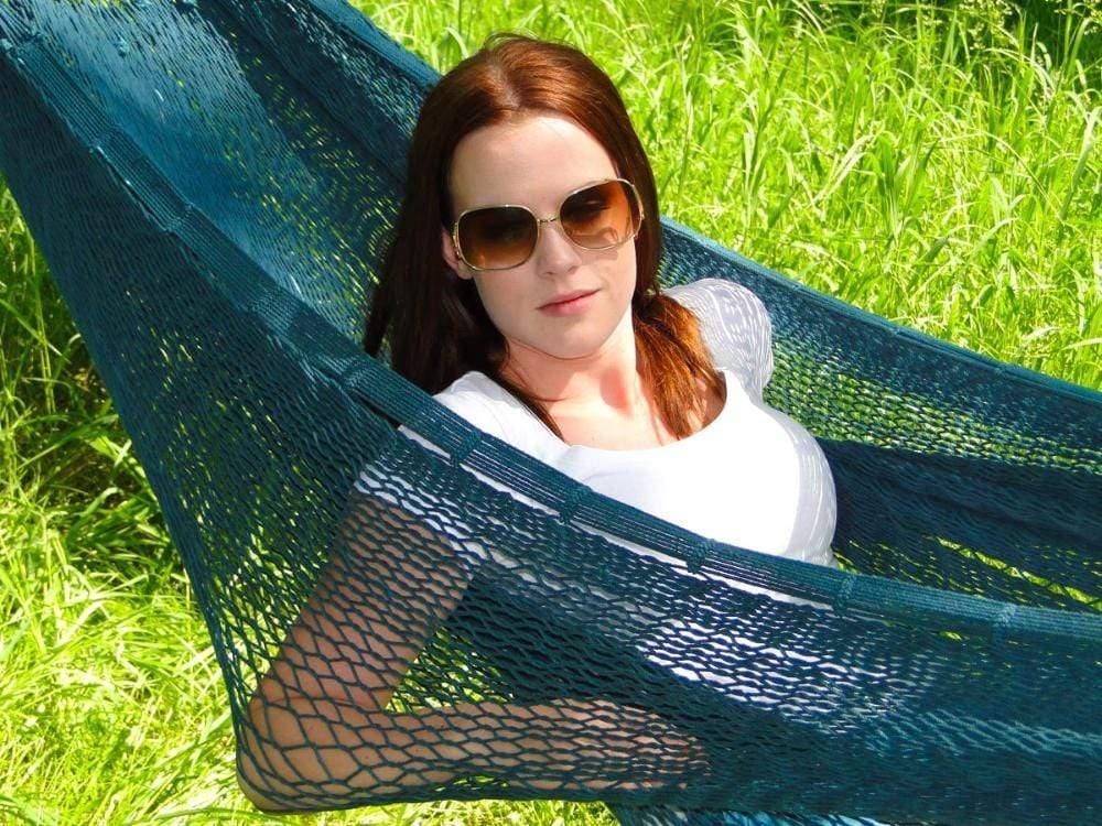 Woman relaxing in forest green Mayan XL hammock outdoors on bright green grass