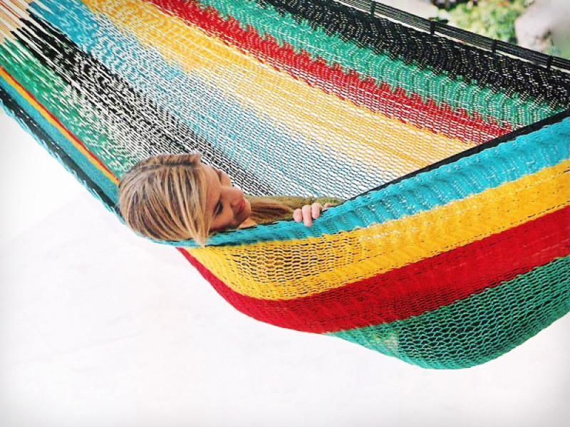 Woman relaxing in a colorful XL Mayan hammock with thick cord on a white patio