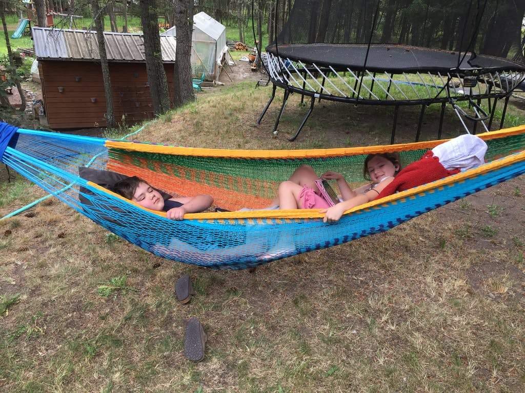 Two children relaxing in a colorful Mayan hammock outdoors near a trampoline