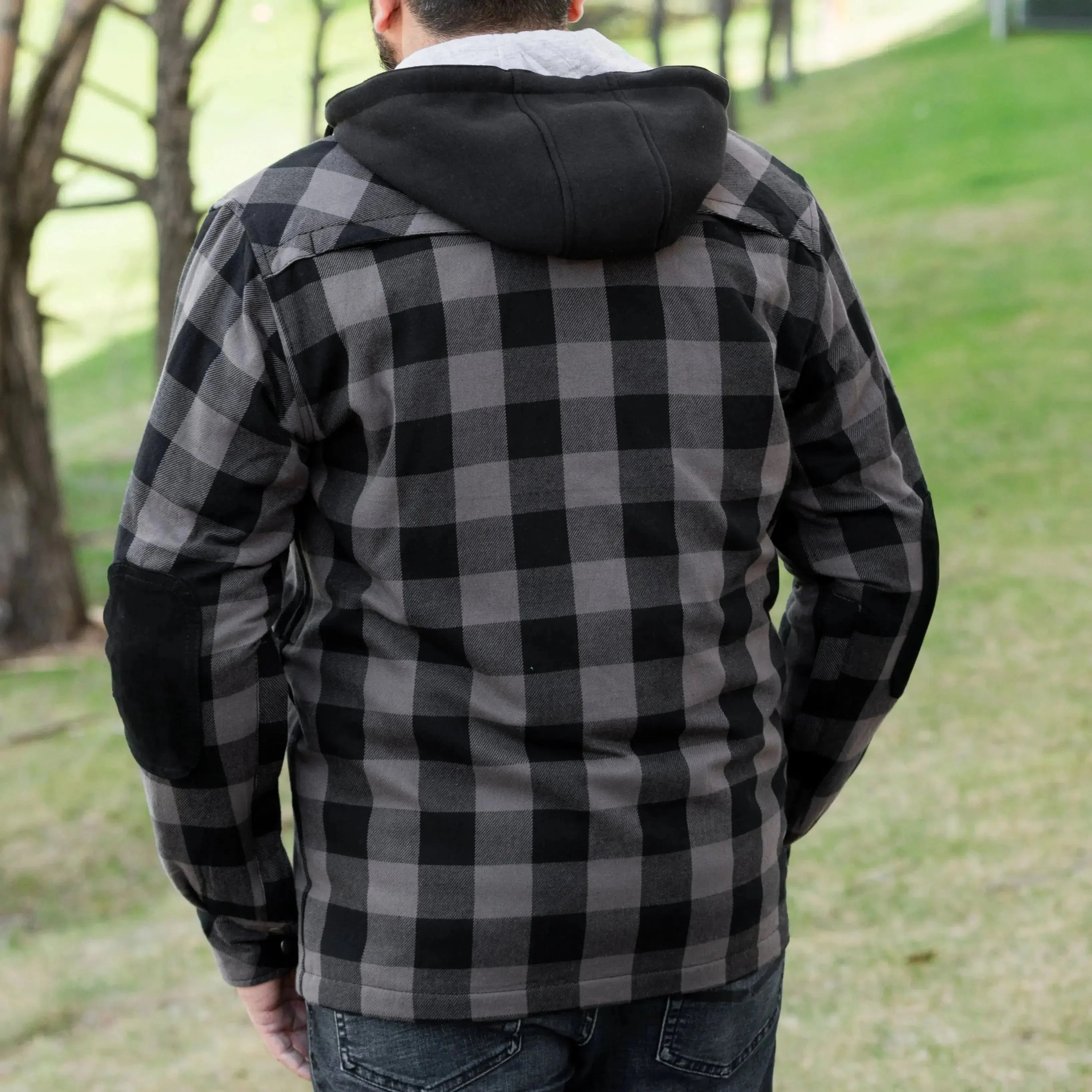 Man in black and grey plaid hooded jacket standing outdoors on grass