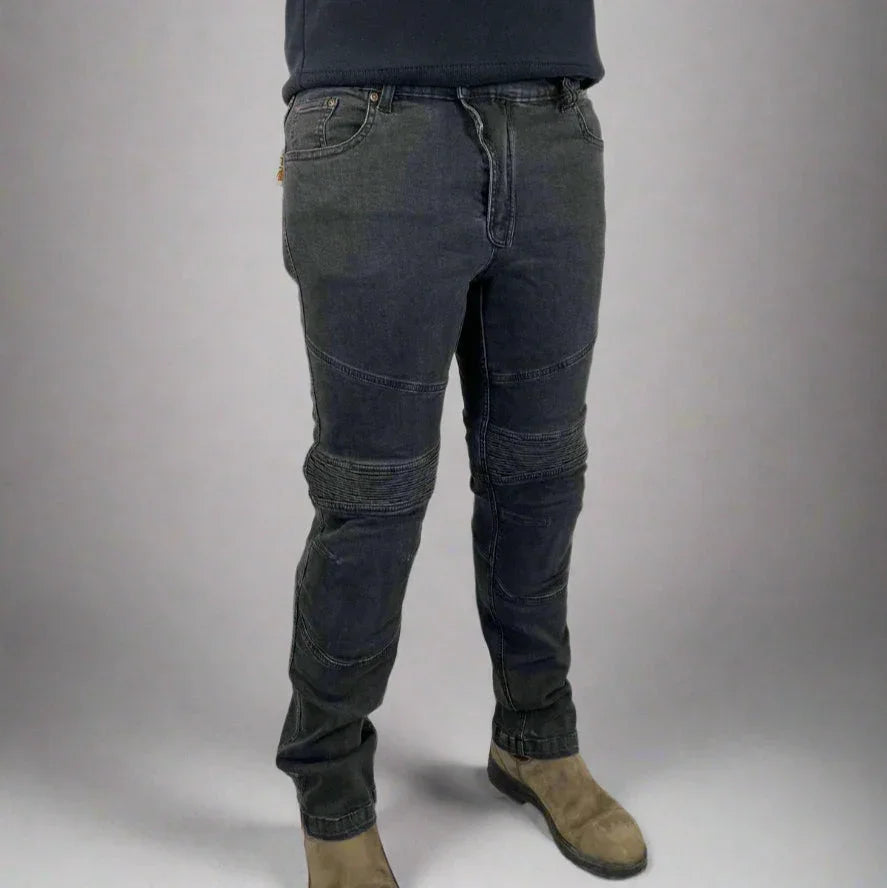 Man wearing black moto jeans with reinforced knee panels and tan boots, studio background