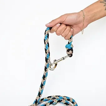 Hand holding braided blue, black, and beige dog leash with metal clasp against white background