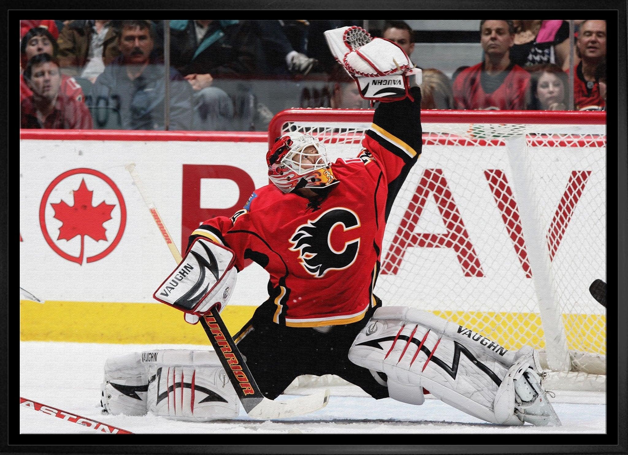 Calgary Flames goalie making glove save in ice hockey game with crowd and net in background
