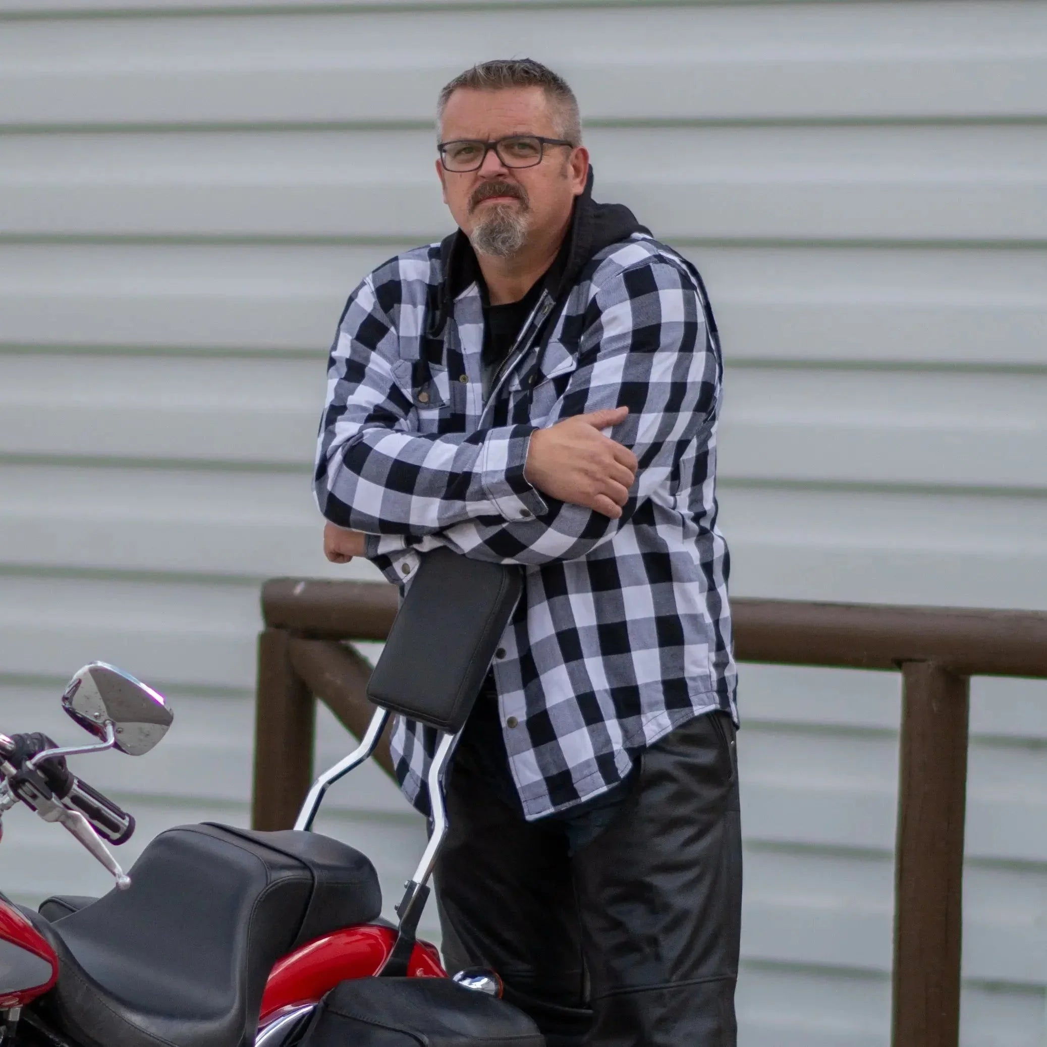 Man in black and white plaid Milwaukee Leather flannel armored shirt by motorcycle outdoors